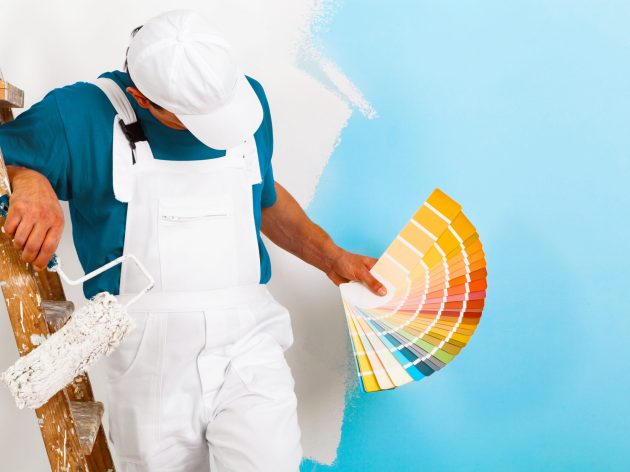 portrait of painter man with paintroller and wooden vintage ladder showing a color palette, on half painted wall