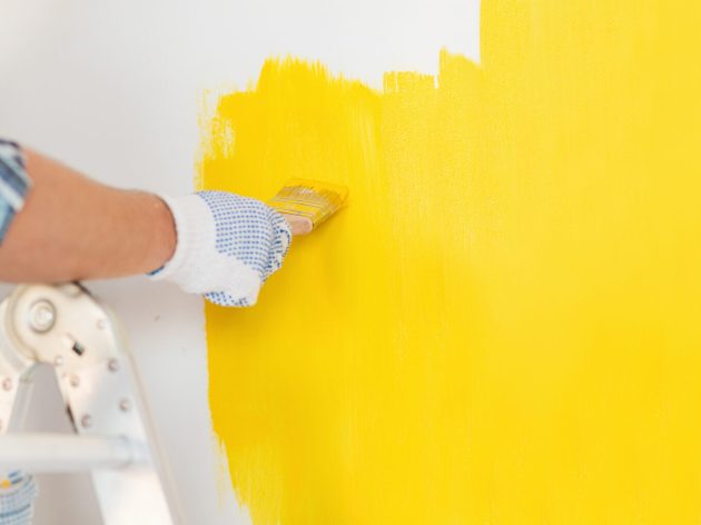 repair and home renovation concept - close up of male hand in gloves painting a wall with yellow paint